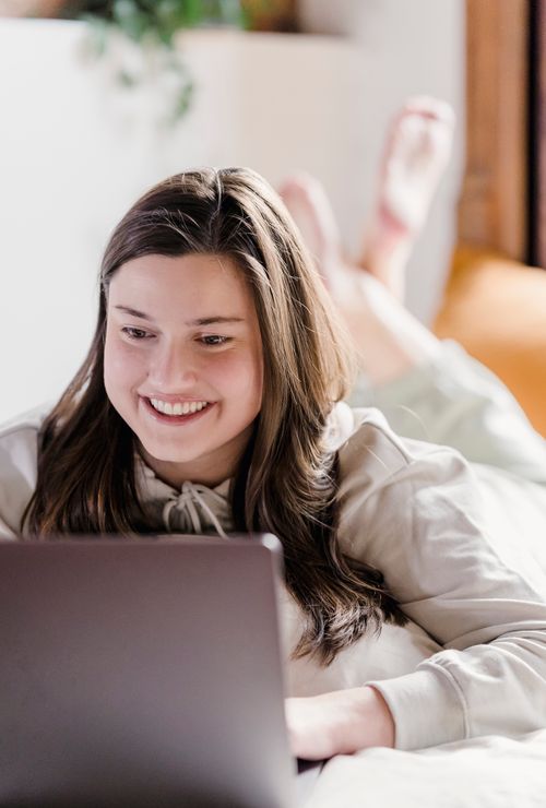 Free Positive female freelancer browsing internet on netbook while lying on soft bed during remote work in bedroom on blurred background Stock Photo