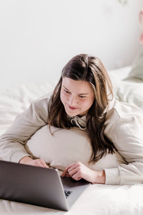 Free Content female freelancer typing on modern netbook while lying on white bed in cozy bedroom during remote work at home Stock Photo