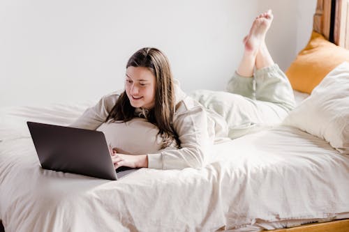 Free Focused woman browsing laptop on soft bed Stock Photo