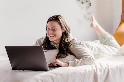 Cheerful woman using laptop on white bed