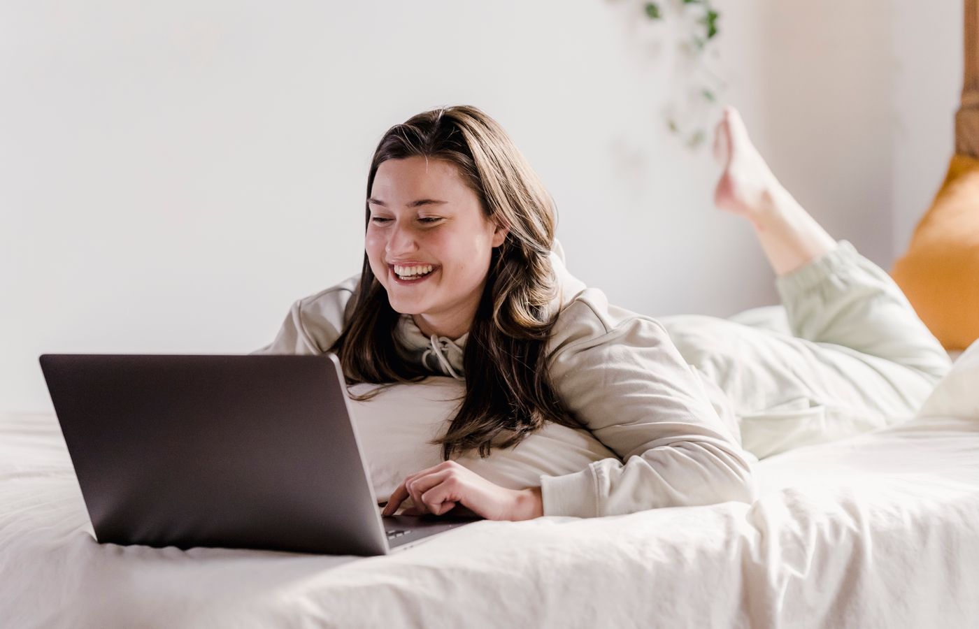 Woman enjoying a relaxed moment browsing on laptop while lying comfortably in a cozy bedroom setting.