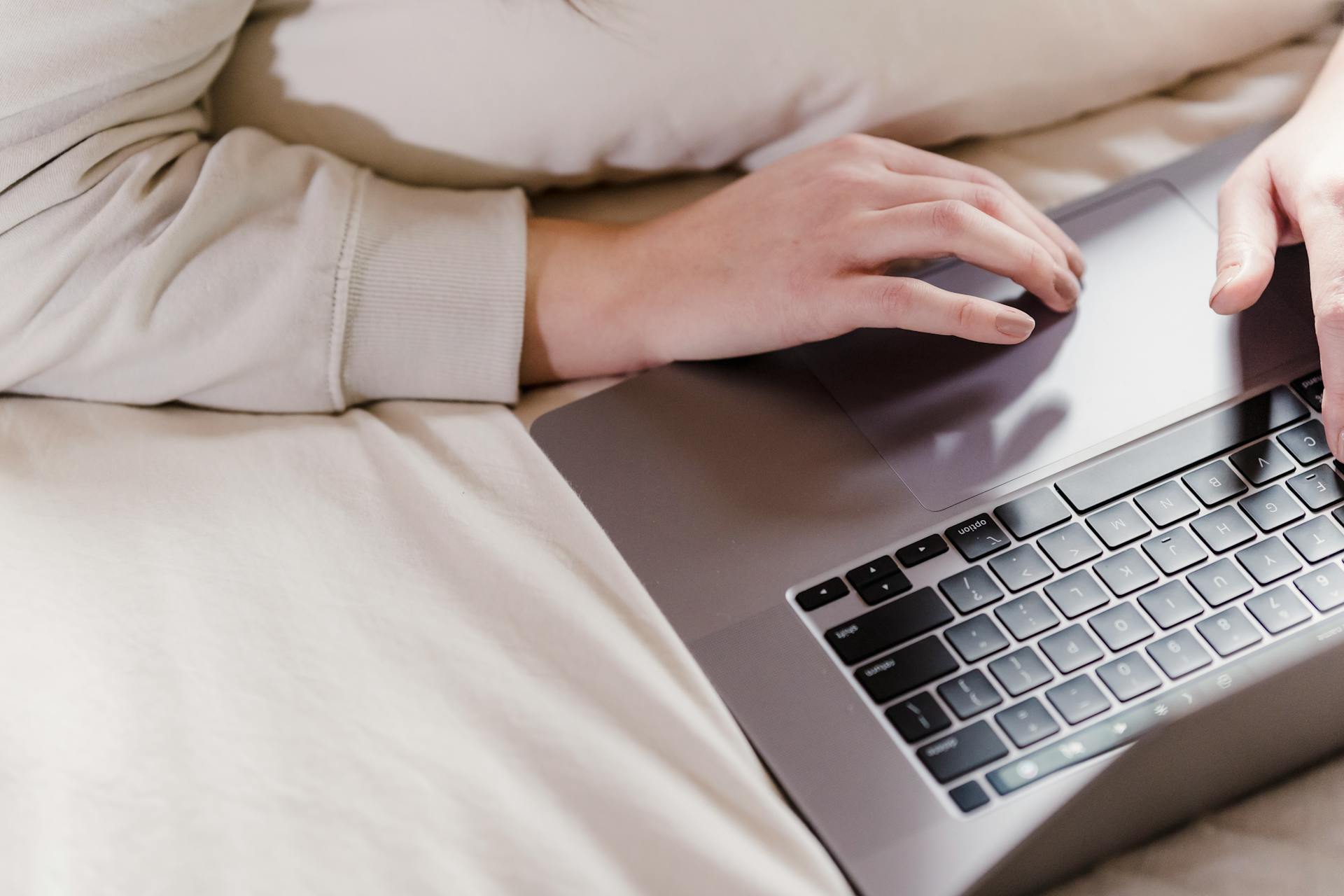 A woman relaxes and works on her laptop in a cozy bedroom environment, showing remote work lifestyle.