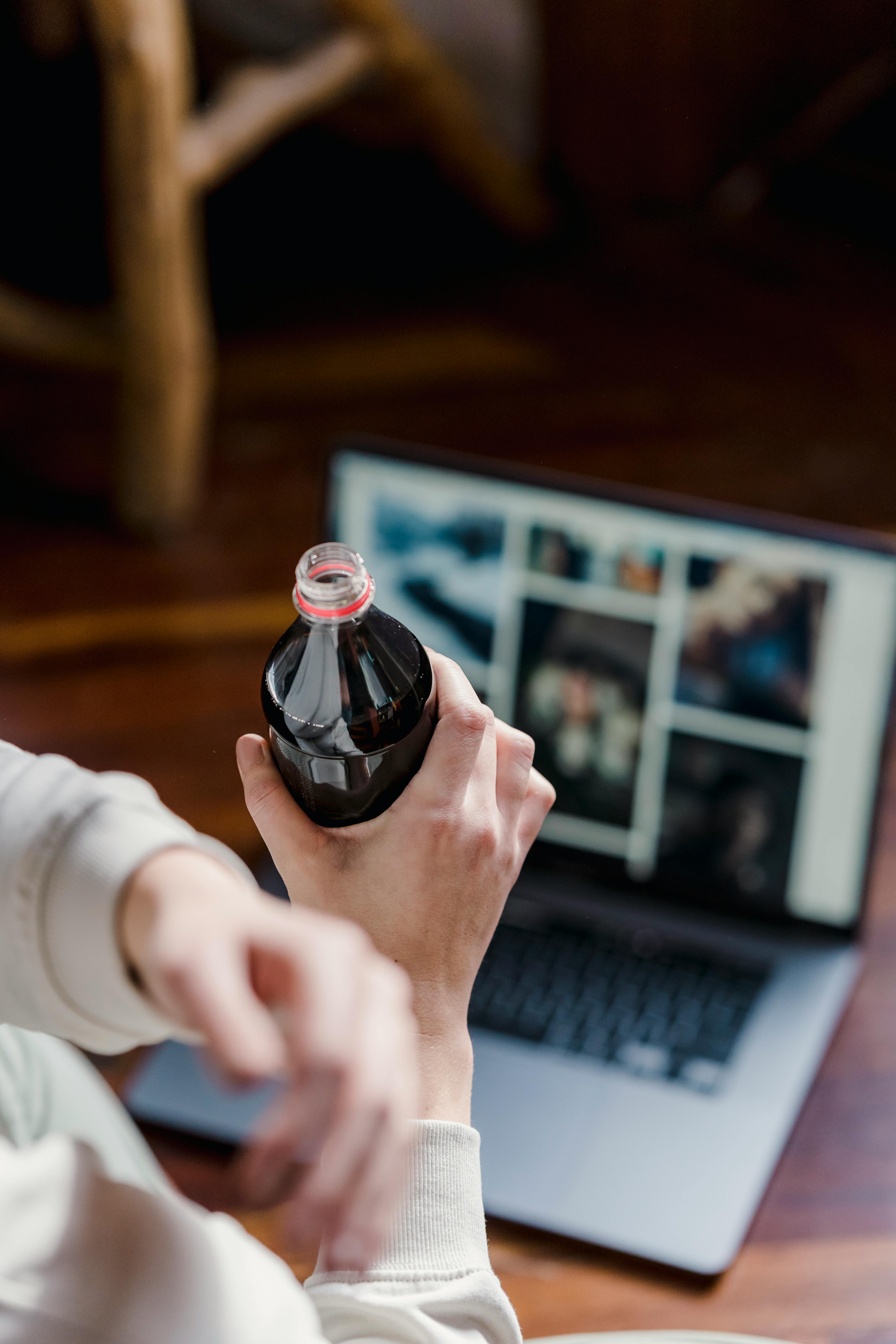 crop person with bottle of drink near netbook