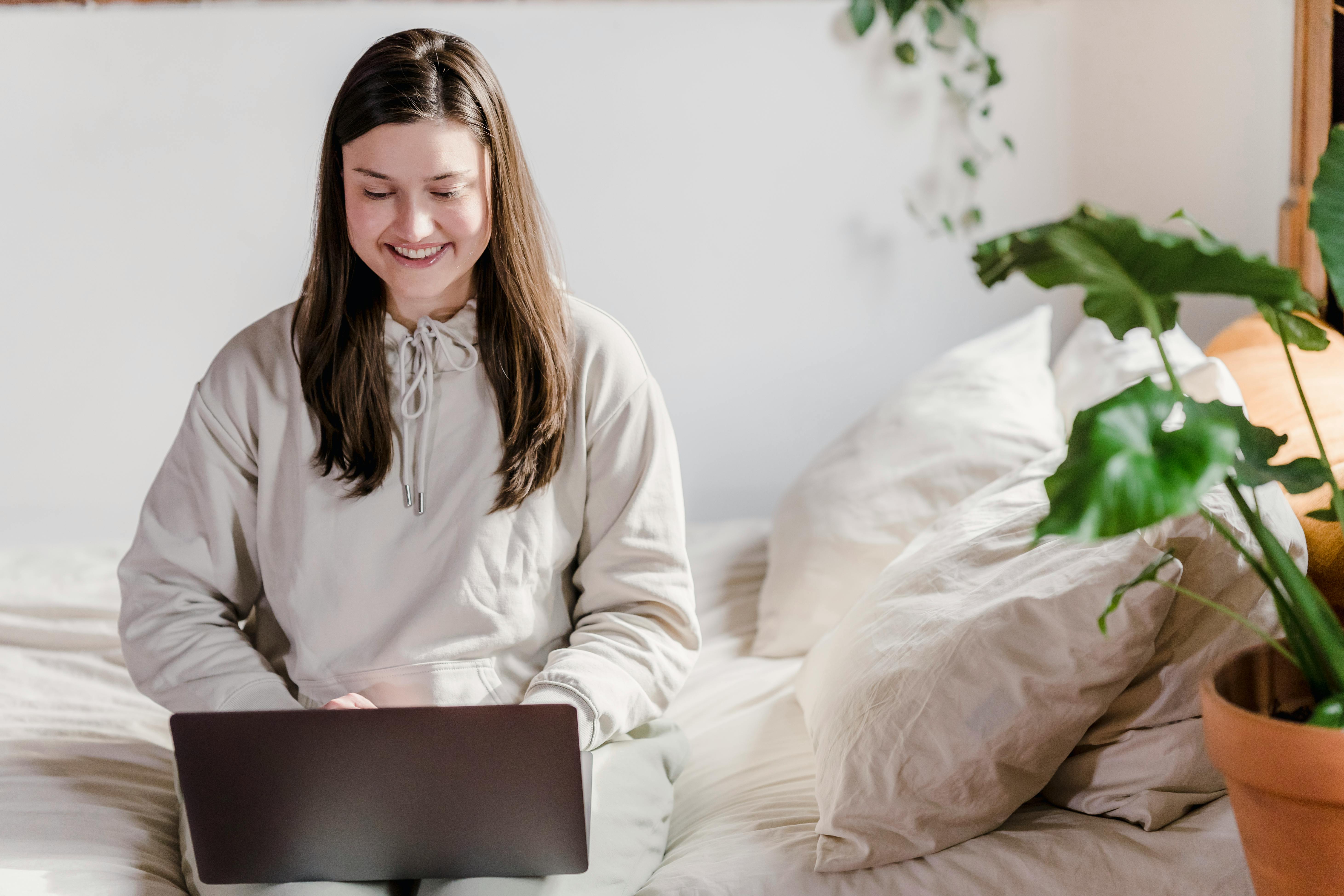 cheerful woman working on laptop in bedroom