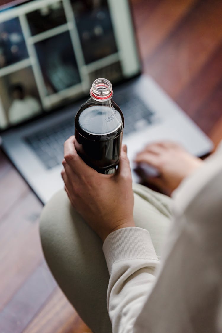 Person Holding Bottle While Surfing Laptop