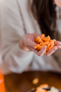 Person holding orange crunchy snack in hand, blurred background.
