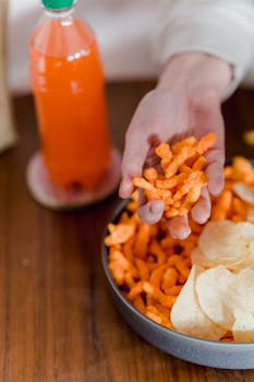 From above of crop anonymous person sitting at table with bottle of soda and eating tasty snacks in daylight