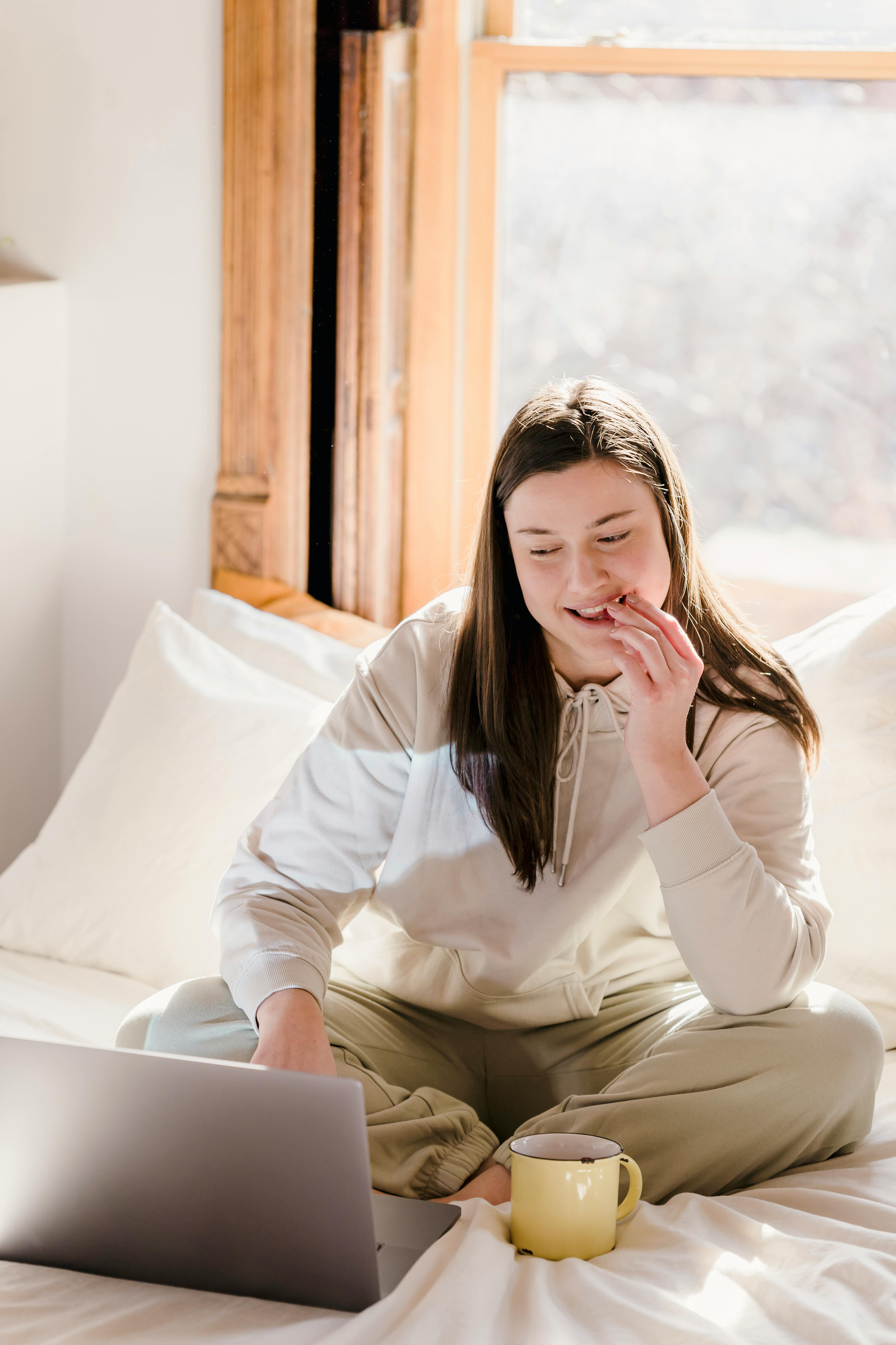 young cheerful woman using laptop while having snack on bed