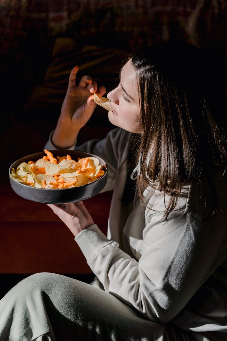 Young Woman Eating Crisps At Home