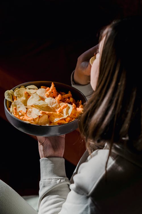 Back view of crop anonymous female enjoying aromatic delicious crusty crisps in plate at home