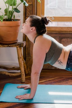 Woman performing yoga stretch on mat near window. Serene indoor setting with natural sunlight.