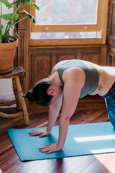 A woman practicing yoga on a mat in a sunlit room with plants, focusing on relaxation and wellness.