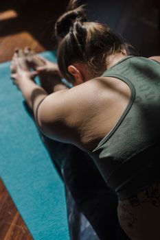 A woman stretches in a yoga pose on a blue mat indoors during the day.