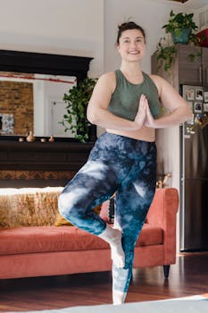 Woman practicing yoga in a cozy living room, striking a tree pose with a smile.