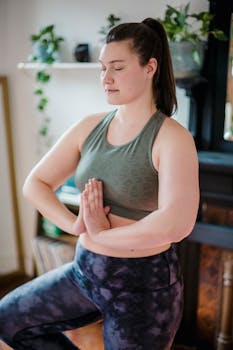 Adult woman meditating in tree pose during home yoga practice, promoting fitness and relaxation.