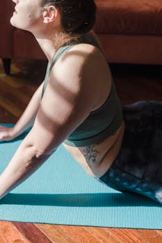 Close-up of a woman performing a yoga stretch on a mat indoors, bathed in natural light.