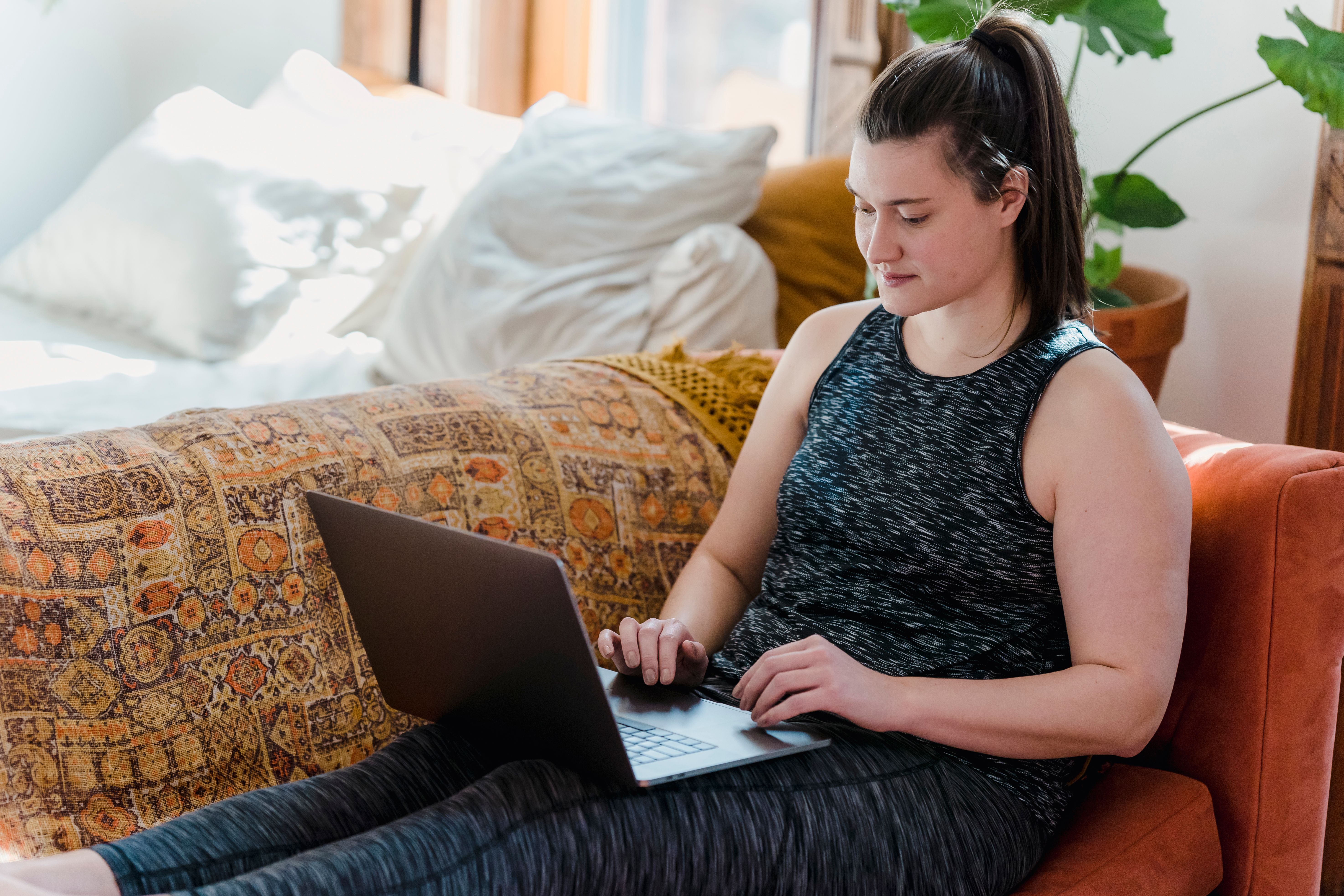 A millennial woman smiling while working on a laptop in a sunny home office with plants