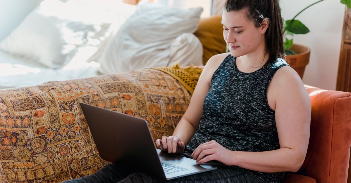 A millennial woman smiling while working on a laptop in a sunny home office with plants