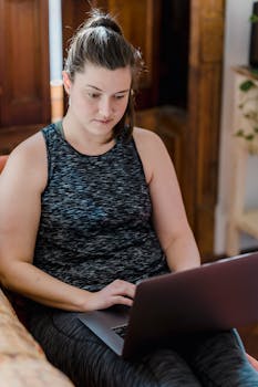 Young woman typing on laptop indoors during the day, focused on screen.