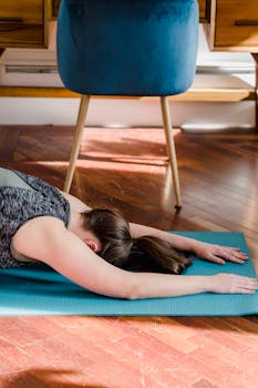 Adult woman performing yoga on a blue mat indoors with natural sunlight.