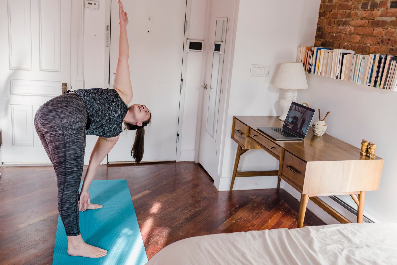 Woman doing an online yoga session on a mat next to her laptop while working from home