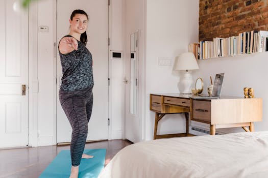 A woman in a bedroom practicing yoga on a mat, surrounded by cozy decor and furniture.