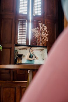 A woman teaching a yoga class via video on a laptop indoors, with natural light.