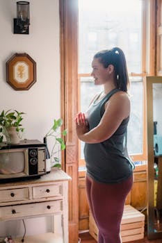 A woman practicing yoga at home by the window with vintage decor and plants nearby.