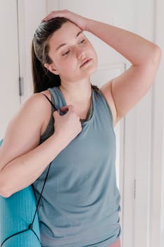A woman indoors relaxing post-yoga, holding a yoga mat with a thoughtful expression.