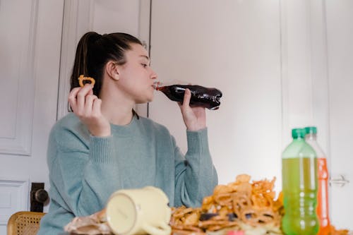 Woman drinking fresh lemonade at table with junk food