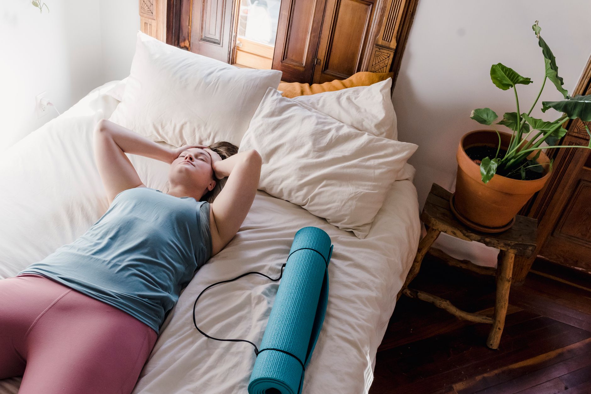 Woman relaxing on bed with yoga mat, enjoying leisure time in a cozy bedroom setting.