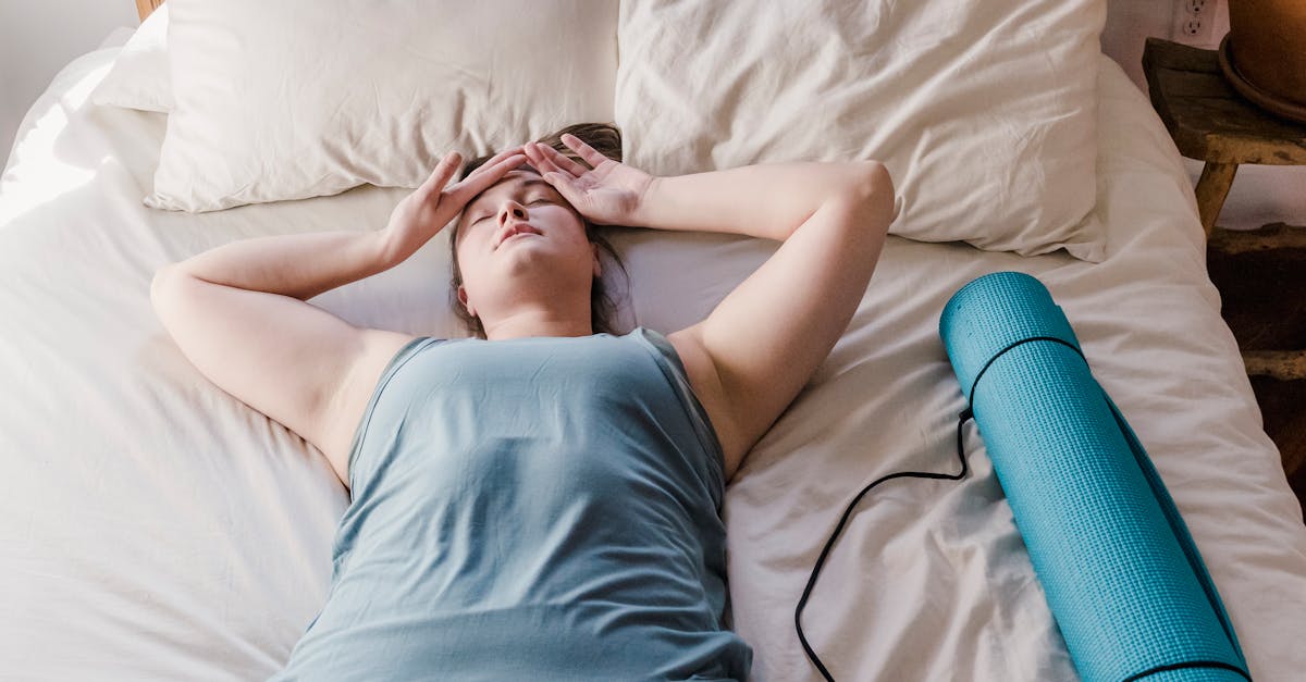 Woman lying on bed with a yoga mat beside her, appearing relaxed and comfortable indoors.