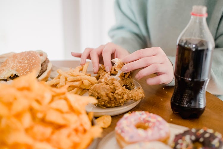 Woman Eating Fried Chicken And Fries At Table With Lemonade