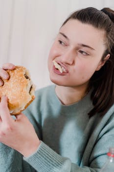 Young crop female with dark hair biting delicious hamburger with cutlet and sesame seeds