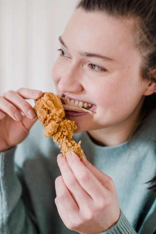 Cheerful smiling young woman eating tasty fried chicken in breading