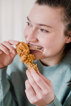 Young woman delightfully eating fried chicken, enjoying a relaxed moment indoors.