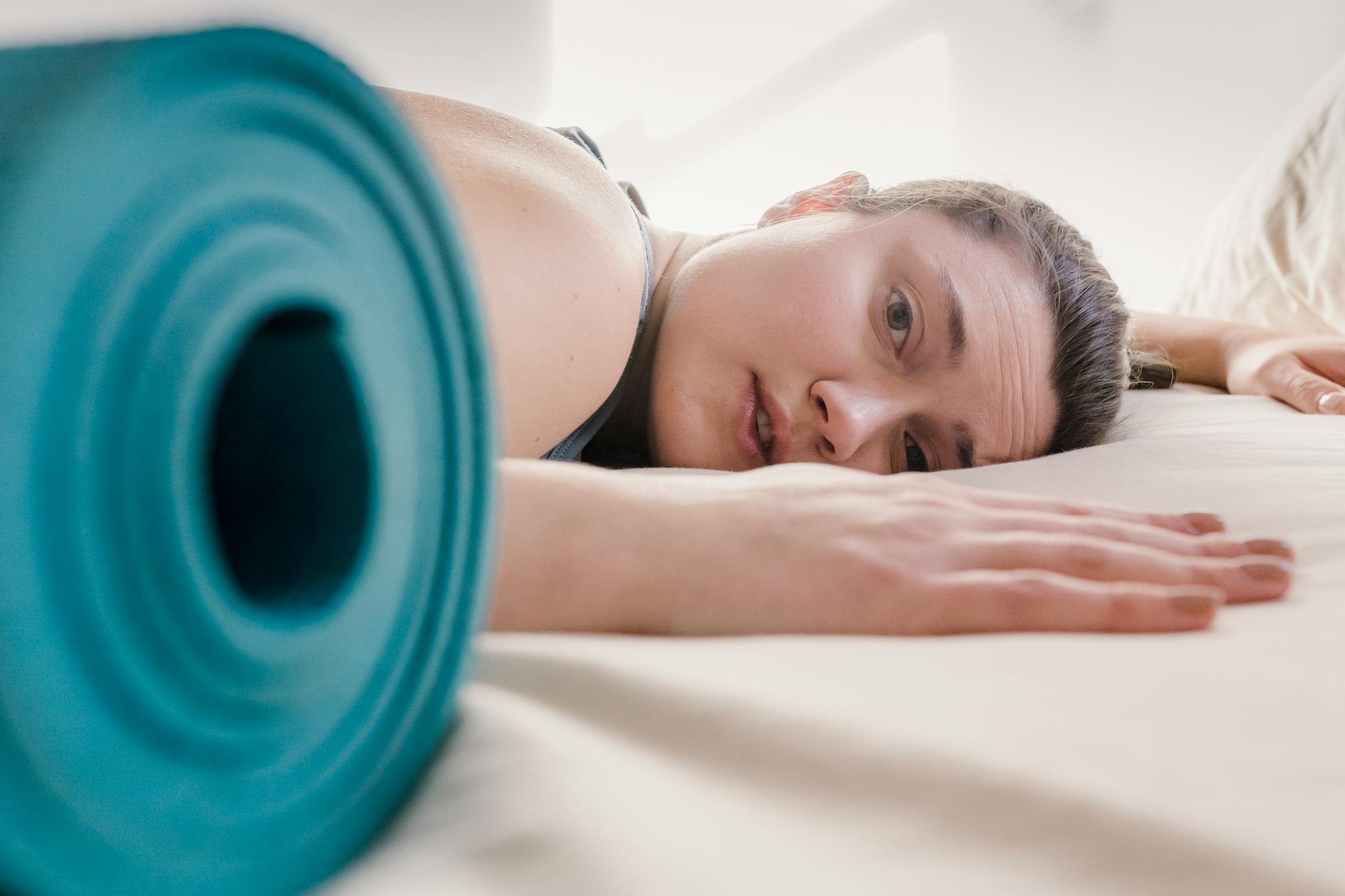 woman lying on ground with rolled up yoga mat