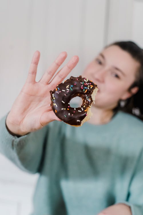 Woman showing bitten donut with chocolate glaze