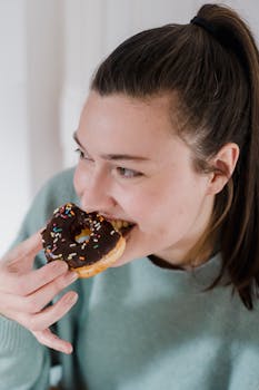 From above of happy young female with dark hair eating yummy doughnut and smiling while looking away