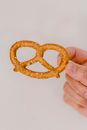 Closeup shot of delicious baked pretzels with salty specks placed in fingers on gray background