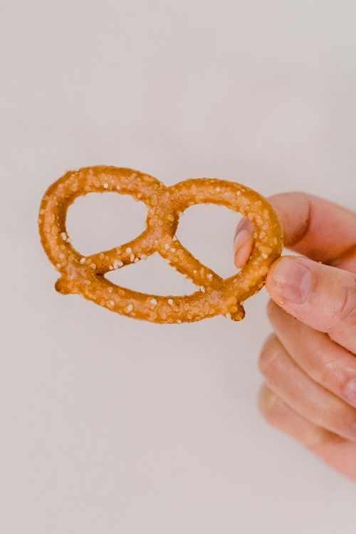 Free Closeup shot of delicious baked pretzels with salty specks placed in fingers on gray background Stock Photo