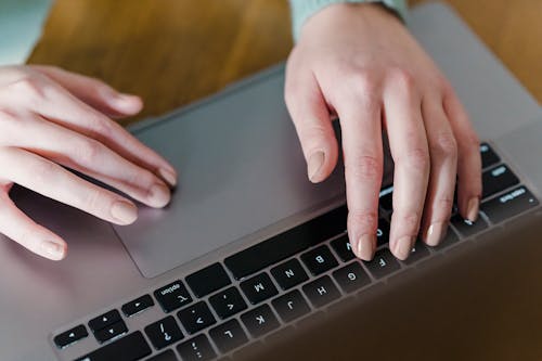 From above of crop person using touchpad of laptop while browsing internet sitting near wooden table