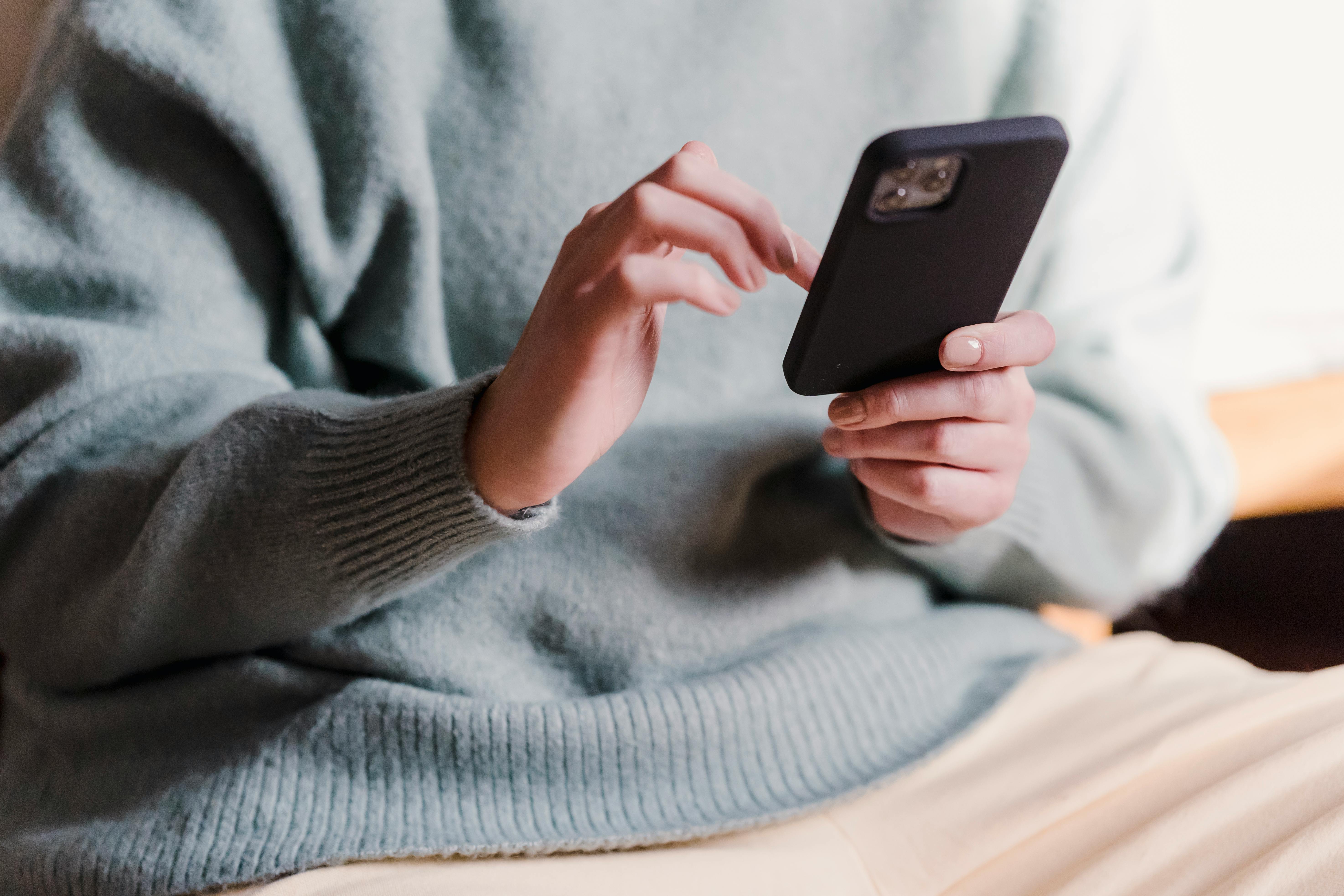 Free Crop faceless female in casual clothes using smartphone and touching screen while chilling at home Stock Photo