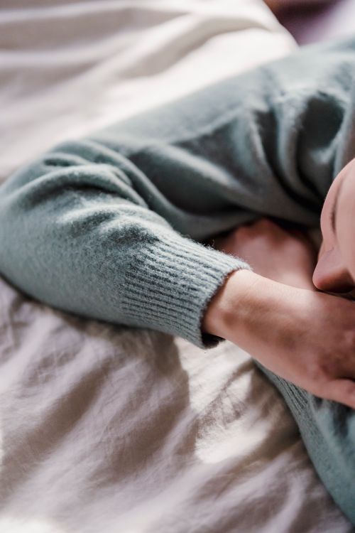 Free Top view of crop unrecognizable female with head on crossed arms in soft gray sweater chilling on comfy sheets Stock Photo