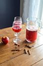 From above of fresh natural juice in glasses and carafe placed on wooden table with whole red apple and aromatic cinnamon sticks