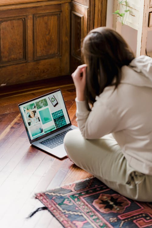 Side view pf unrecognizable self employed woman in casual clothes sitting on floor at home and working remotely on laptop