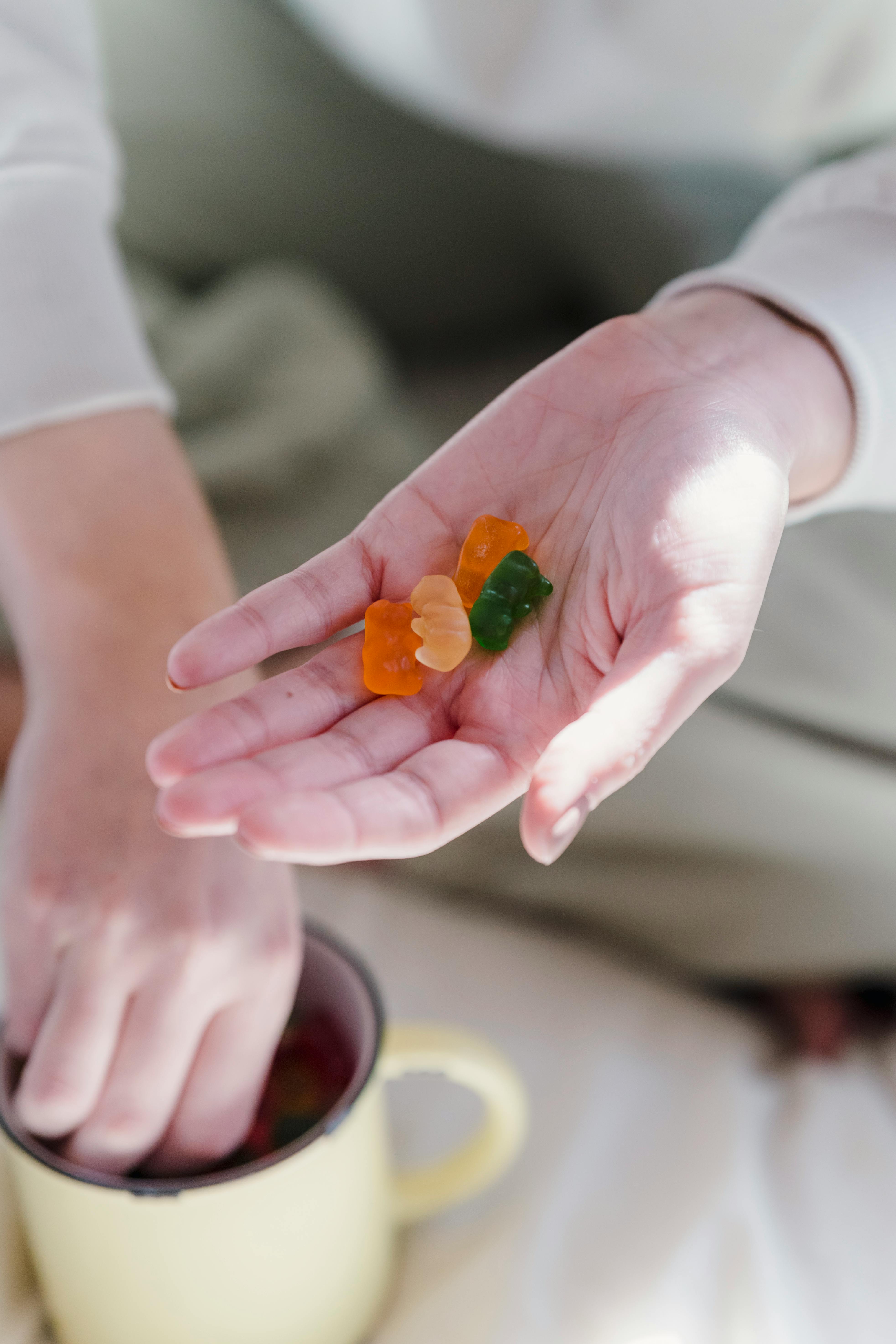 faceless woman showing sweet gummy candies while sitting on bed in morning