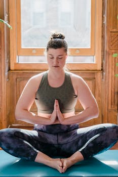 Woman meditating on a yoga mat indoors, embracing calm and relaxation.