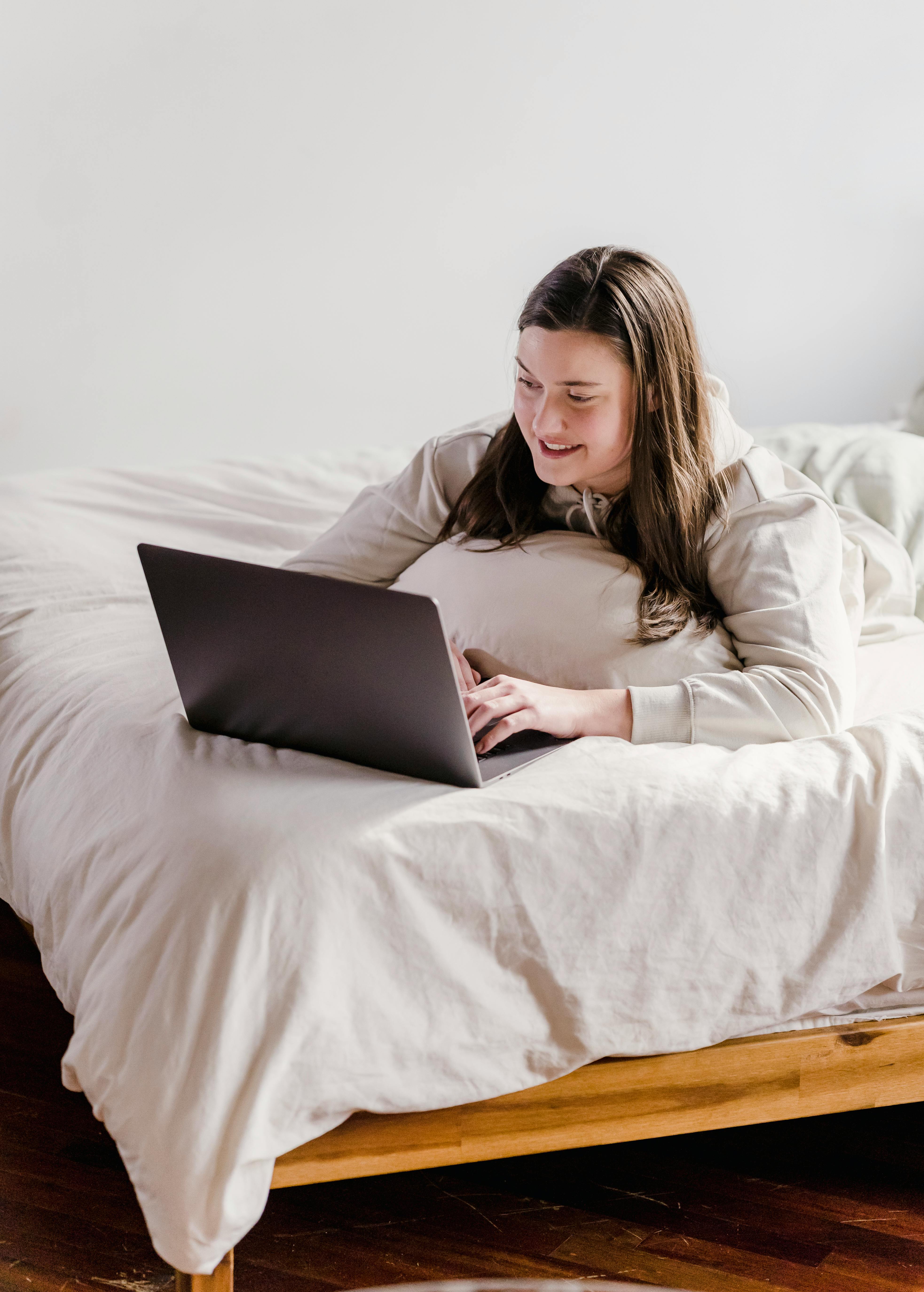 positive young lady relaxing on bed and watching movie on laptop