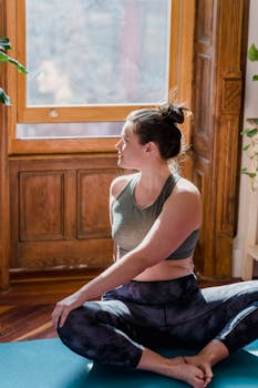 Woman practicing yoga seated by a window, embracing a peaceful and mindful lifestyle at home.